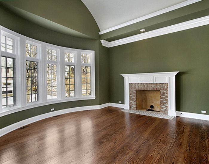 Empty room with green walls, curved window, fireplace, and hardwood floors.