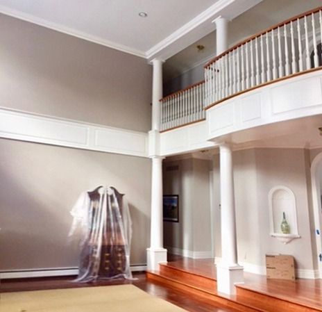 Spacious interior with columns, balcony, and hardwood floors; beige walls and white trim.