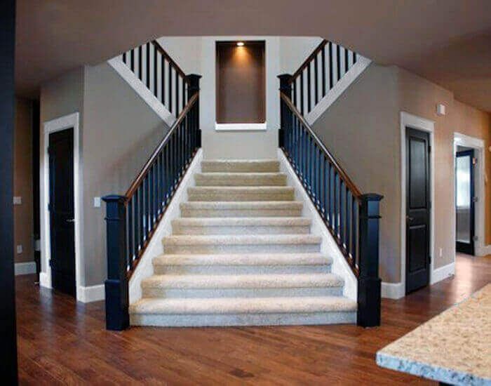 A grand staircase with carpeted steps, black railing, and a central display niche, leading upwards.