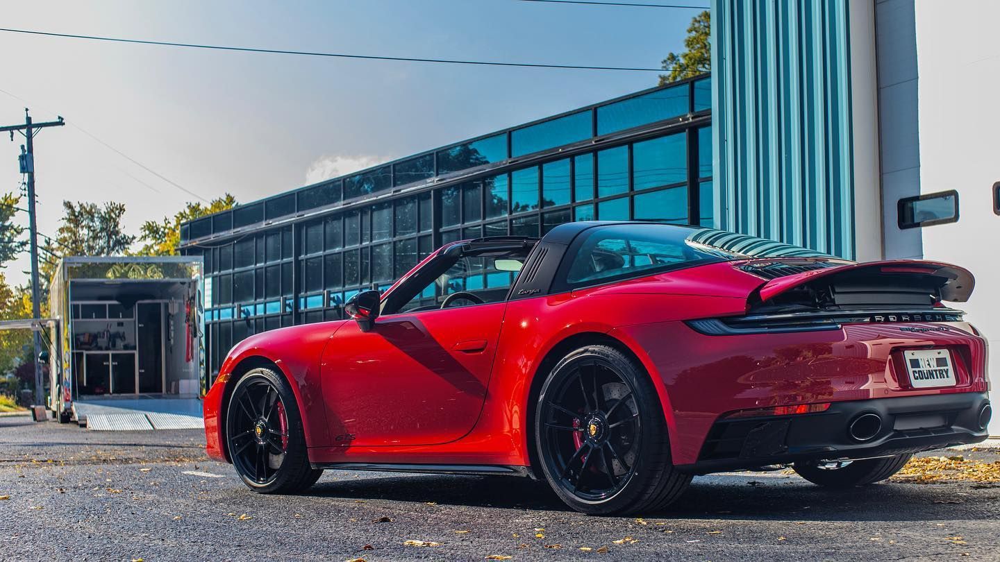 a red porsche 911 targa is parked in front of a building .