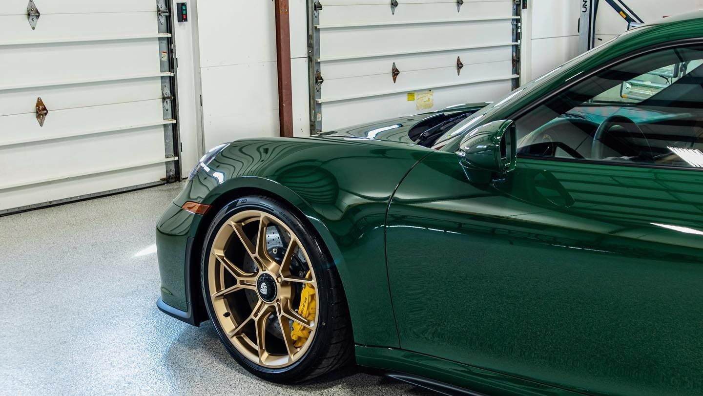 a green sports car with gold wheels is parked in a garage .