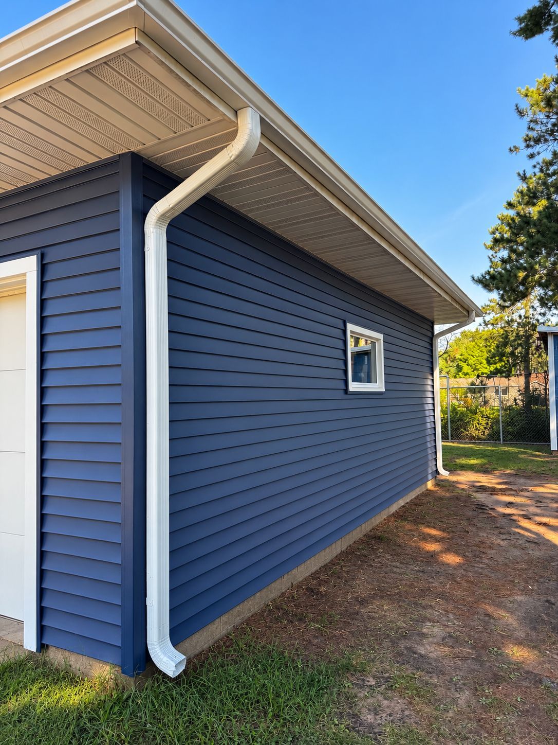 Blue house exterior with white trim, a small window, and a white downspout along the side wall.