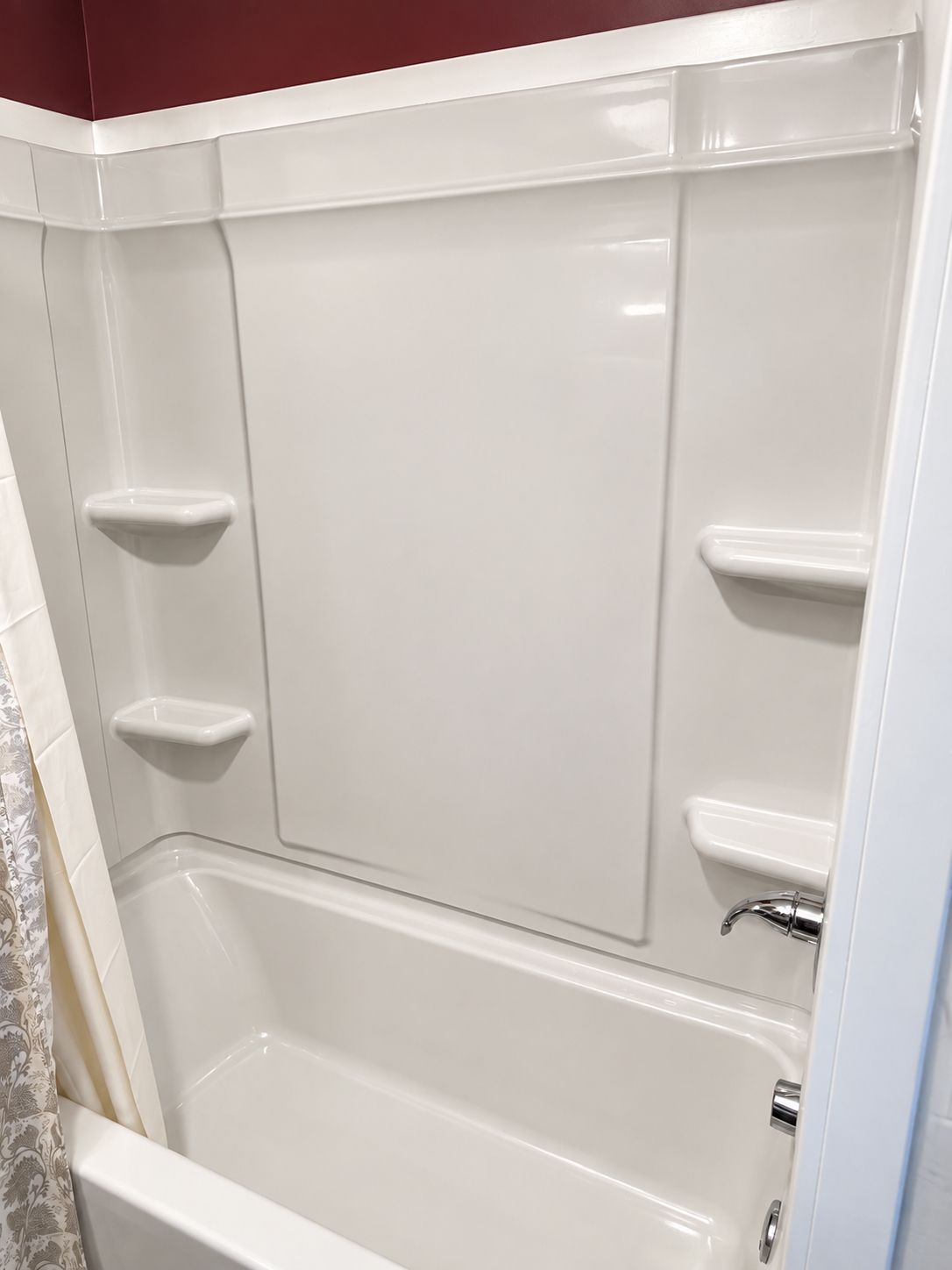White bathtub and shower surround with built-in corner shelves and a handheld showerhead.