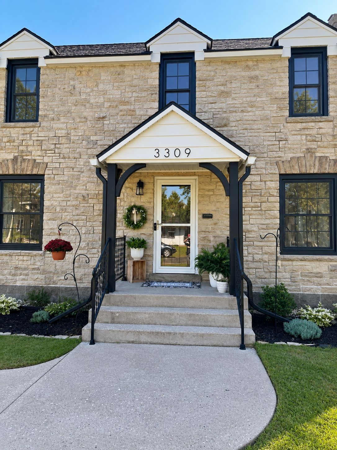 Stone house front entrance with black-trimmed windows, white awning, and curved concrete walkway.