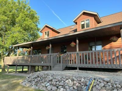 Brick house with covered porch, wooden railing, and rock landscaping under a blue sky
