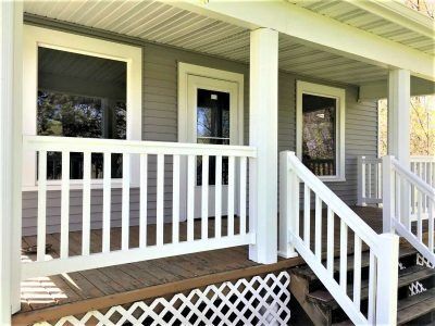 Front porch with white railing, green siding, dark doors, and steps leading up to the entrance.
