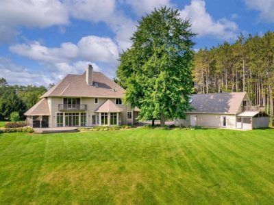 Large house with a green lawn, tall trees, and blue sky with clouds