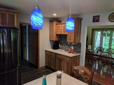 Modern kitchen with stainless fridge, wood cabinets, blue pendant lights, and dining room beyond.