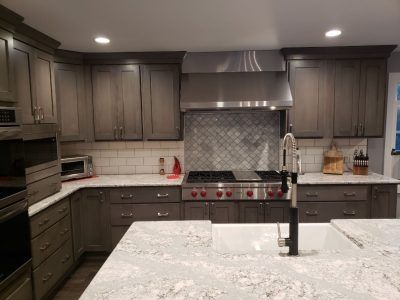Modern kitchen with gray cabinets, stainless steel appliances, and a large white island in front.