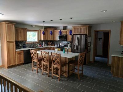 Modern kitchen with wood cabinets, island table, pendant lights, stainless fridge, and dark tile floor