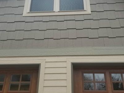 House exterior with gray shingle siding, beige trim, and two windows above a wooden door and lower window.
