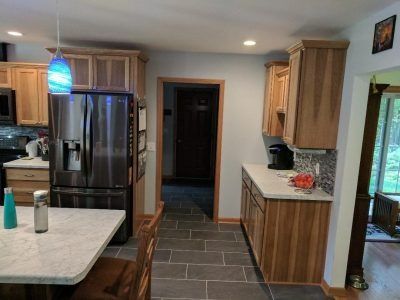 Kitchen with stainless steel fridge, wood cabinets, and tiled floor leading to a hallway