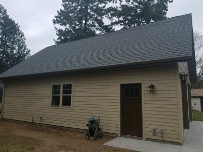 Tan beige house with dark roof, front door, windows, and a lawn mower by the wall
