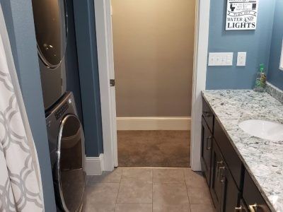 Kitchen with granite counter, dark cabinets, washer and dryer, and a hallway leading to carpeted room.