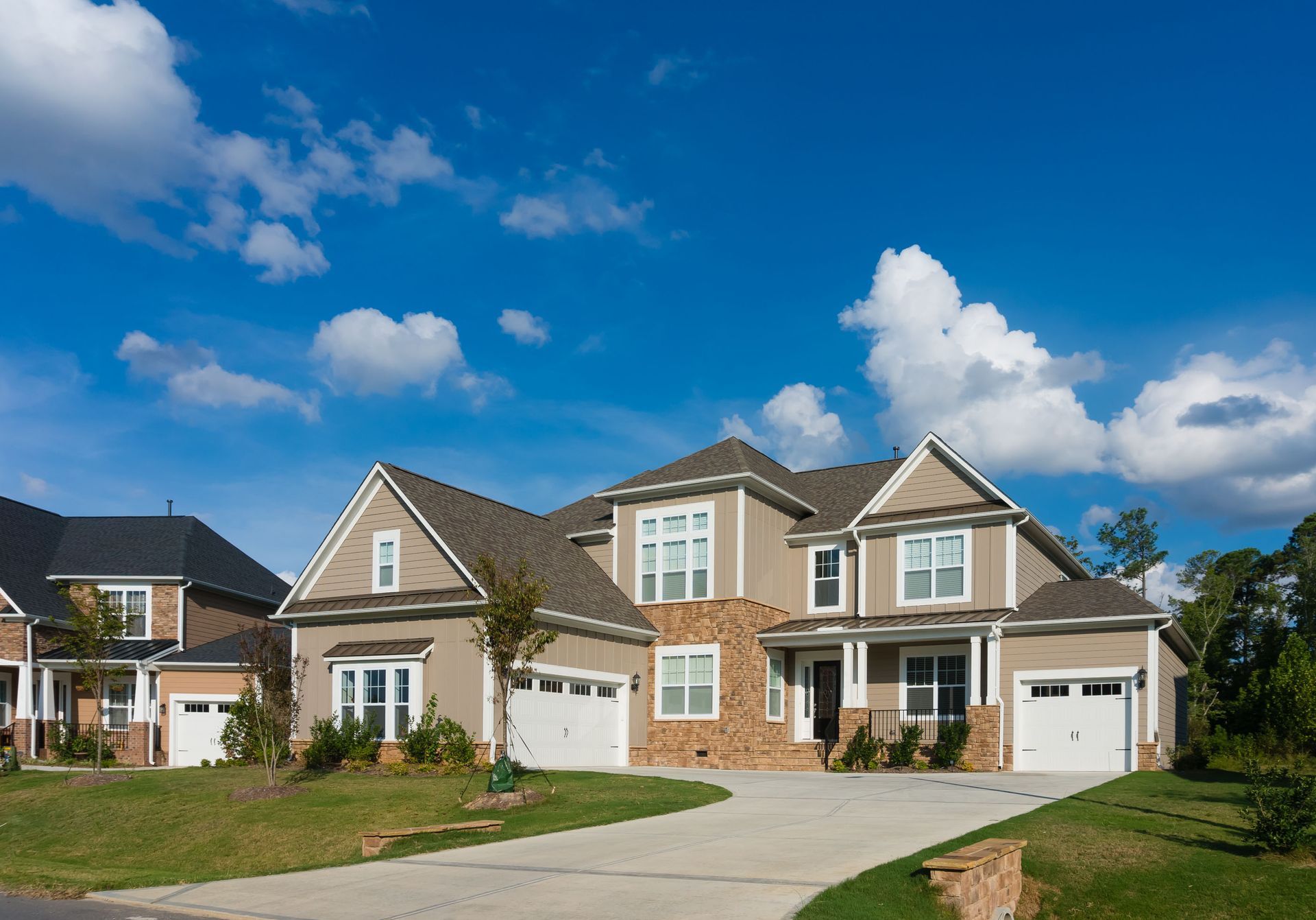Suburban homes with brick and beige facades under a blue sky, viewed from a curved driveway
