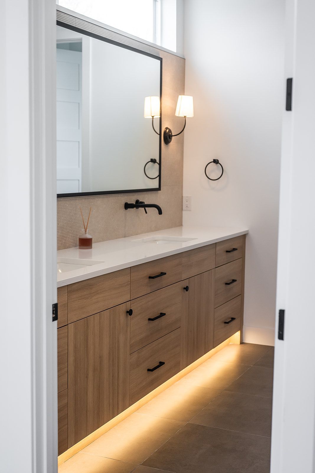 Bathroom with wood vanity, large mirror, black fixtures, and under-cabinet lighting.