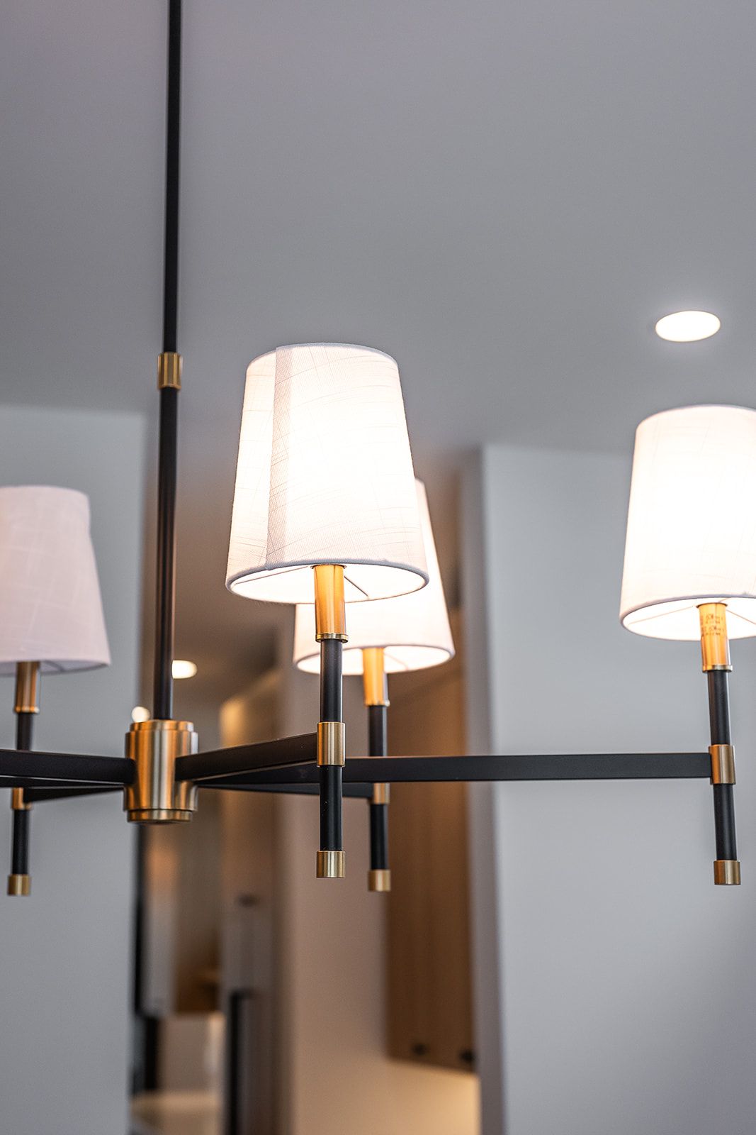 Black and gold chandelier with white lampshades, mounted on a ceiling.