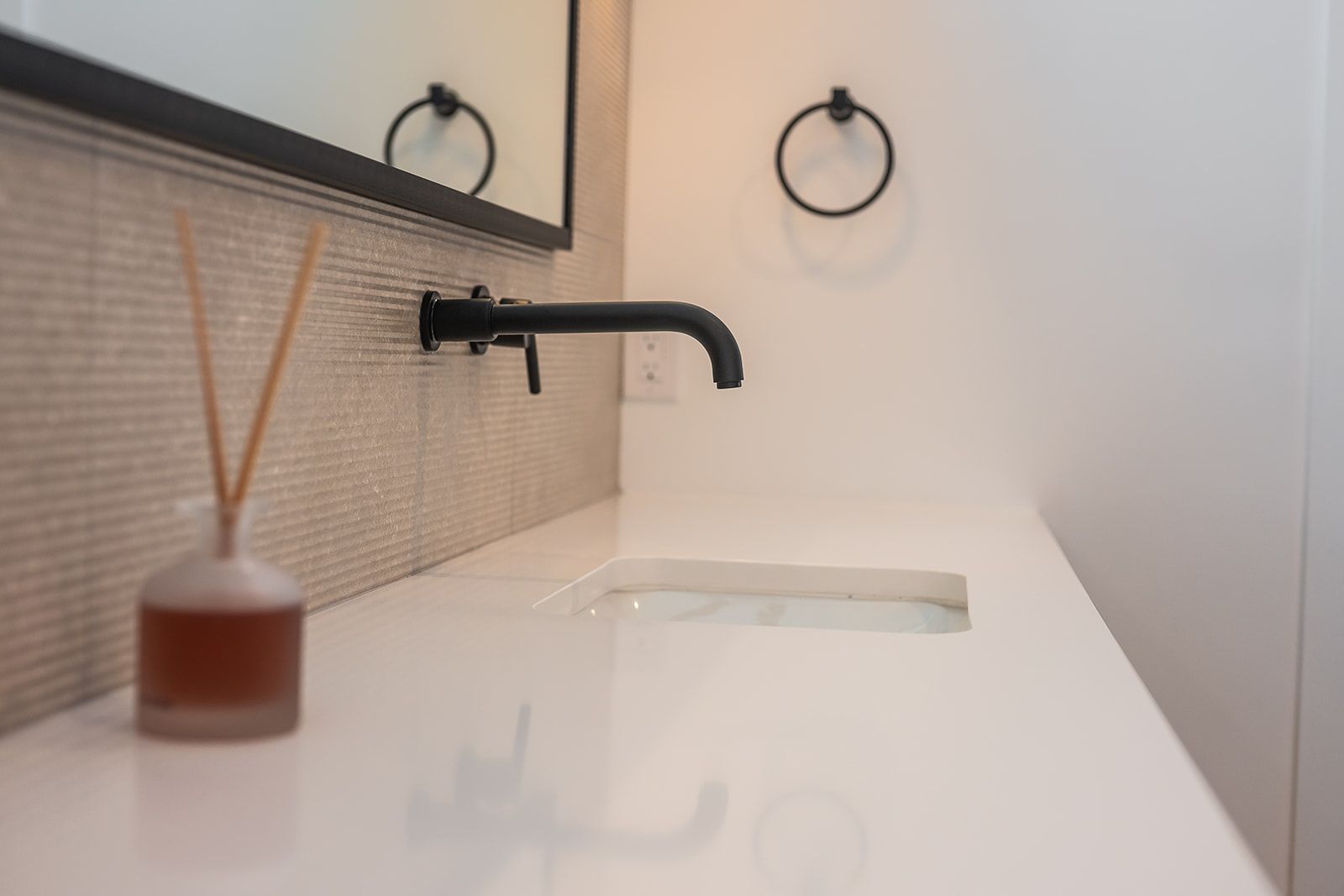 Modern bathroom vanity with a black faucet, white countertop, and reed diffuser.