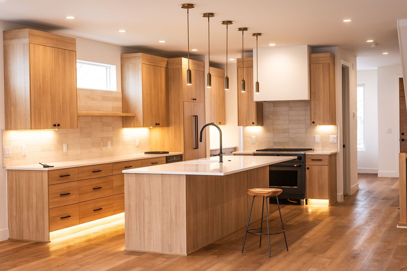 Modern kitchen with light wood cabinets, island, black accents, and pendant lights.