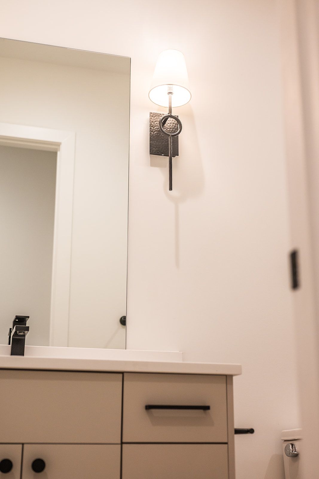 Bathroom vanity with mirror, light fixture, and black hardware on a white wall.