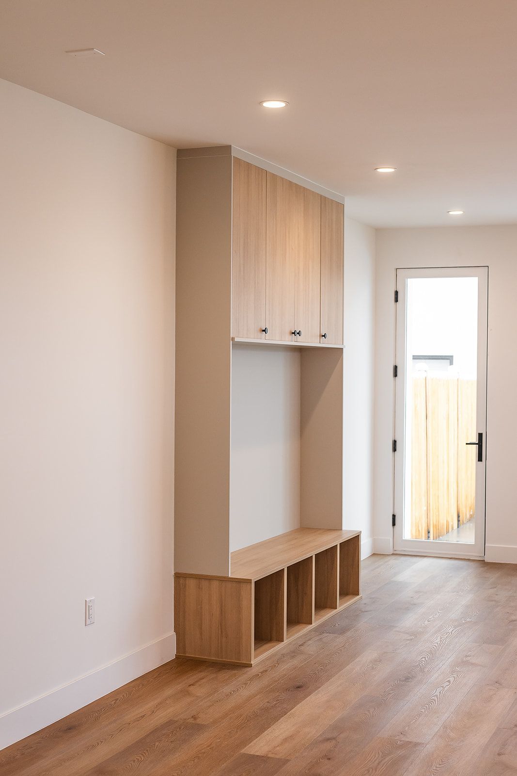 Built-in entryway bench with storage and upper cabinets; wooden floors and white walls.