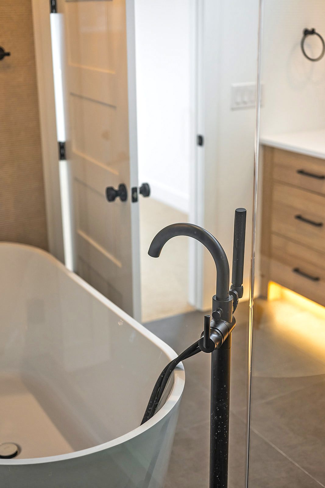 Freestanding bathtub and black faucet in a modern bathroom, open door to adjacent room.