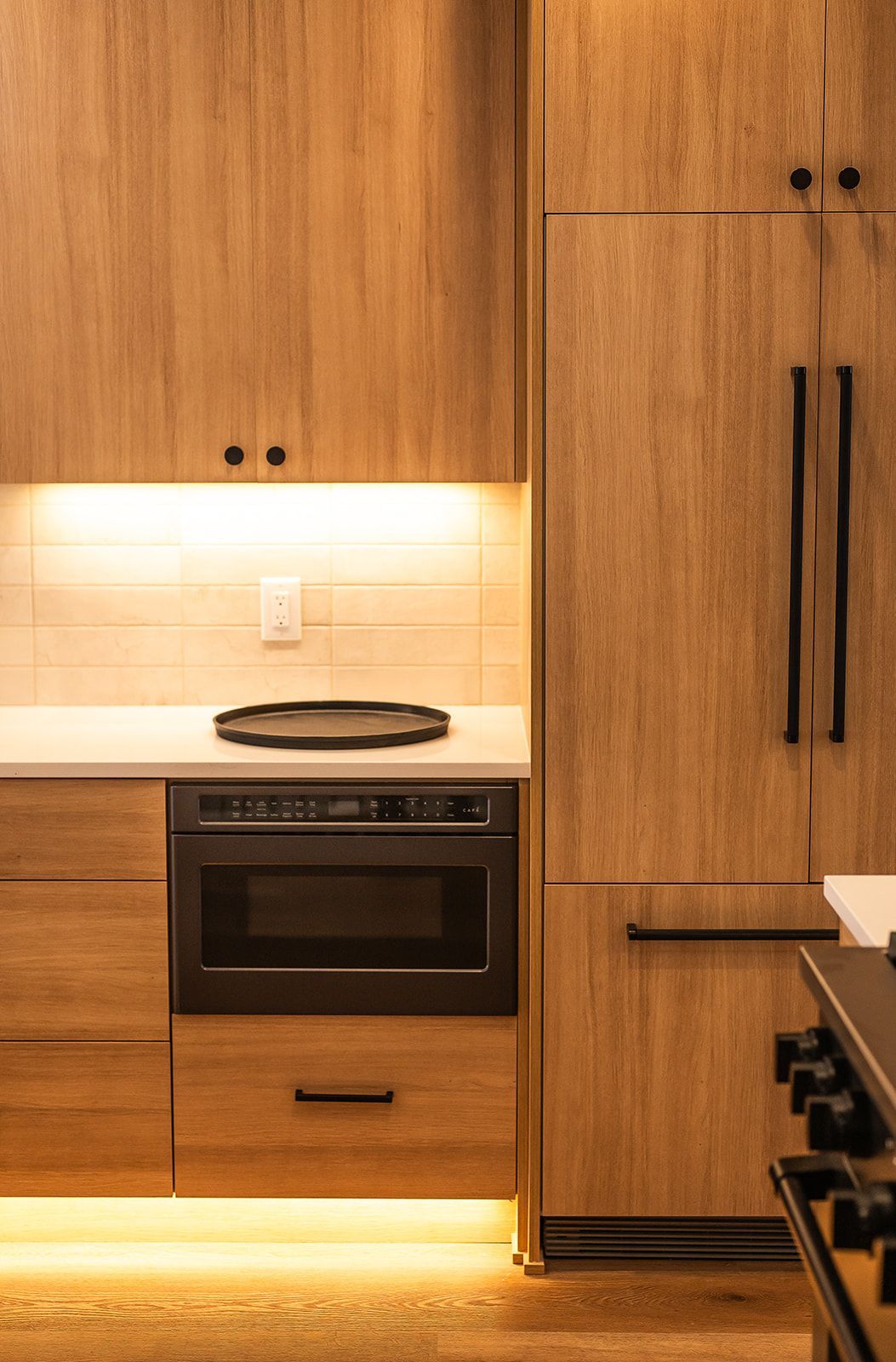 Wooden kitchen cabinets with a built-in microwave and refrigerator. Soft lighting under the counters.