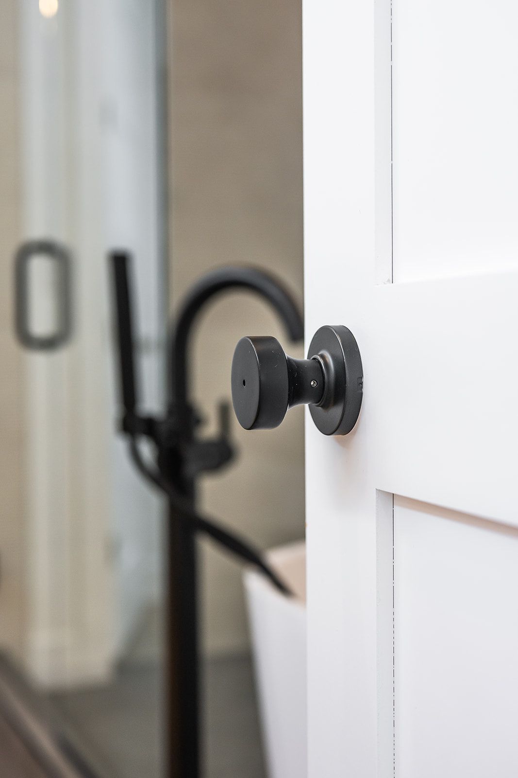 Black doorknob on white door, bathroom in background with black faucet and glass shower.