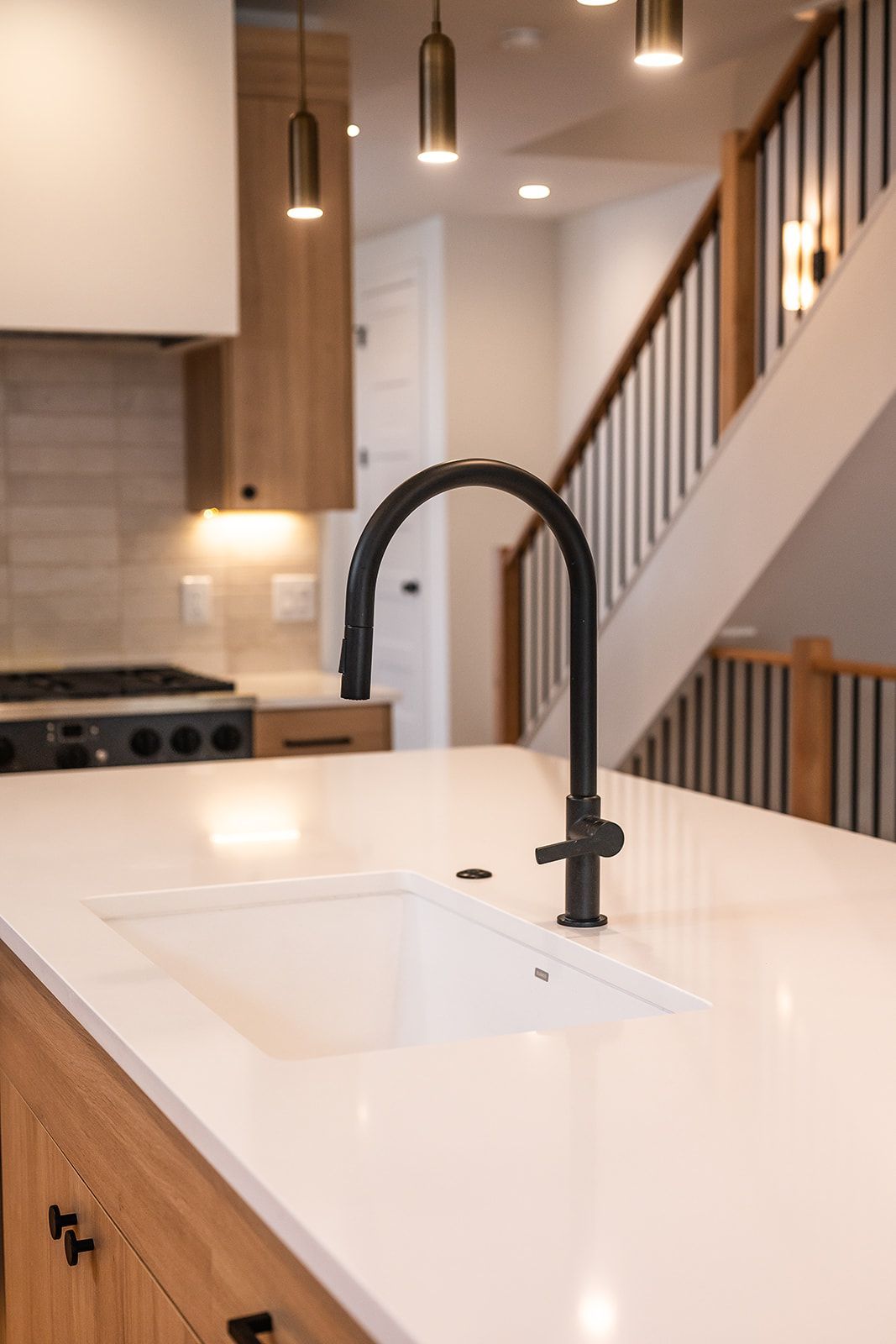 Kitchen island with a black faucet, white sink and countertop, and wooden cabinets. Staircase visible in the background.
