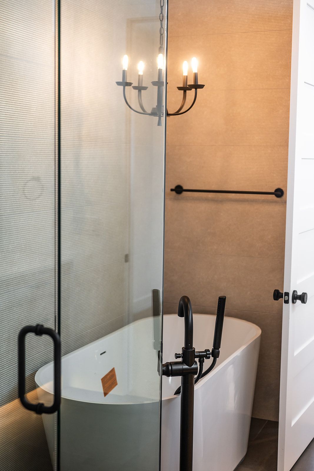 Modern bathroom with a white freestanding tub, glass shower, chandelier, and black fixtures.