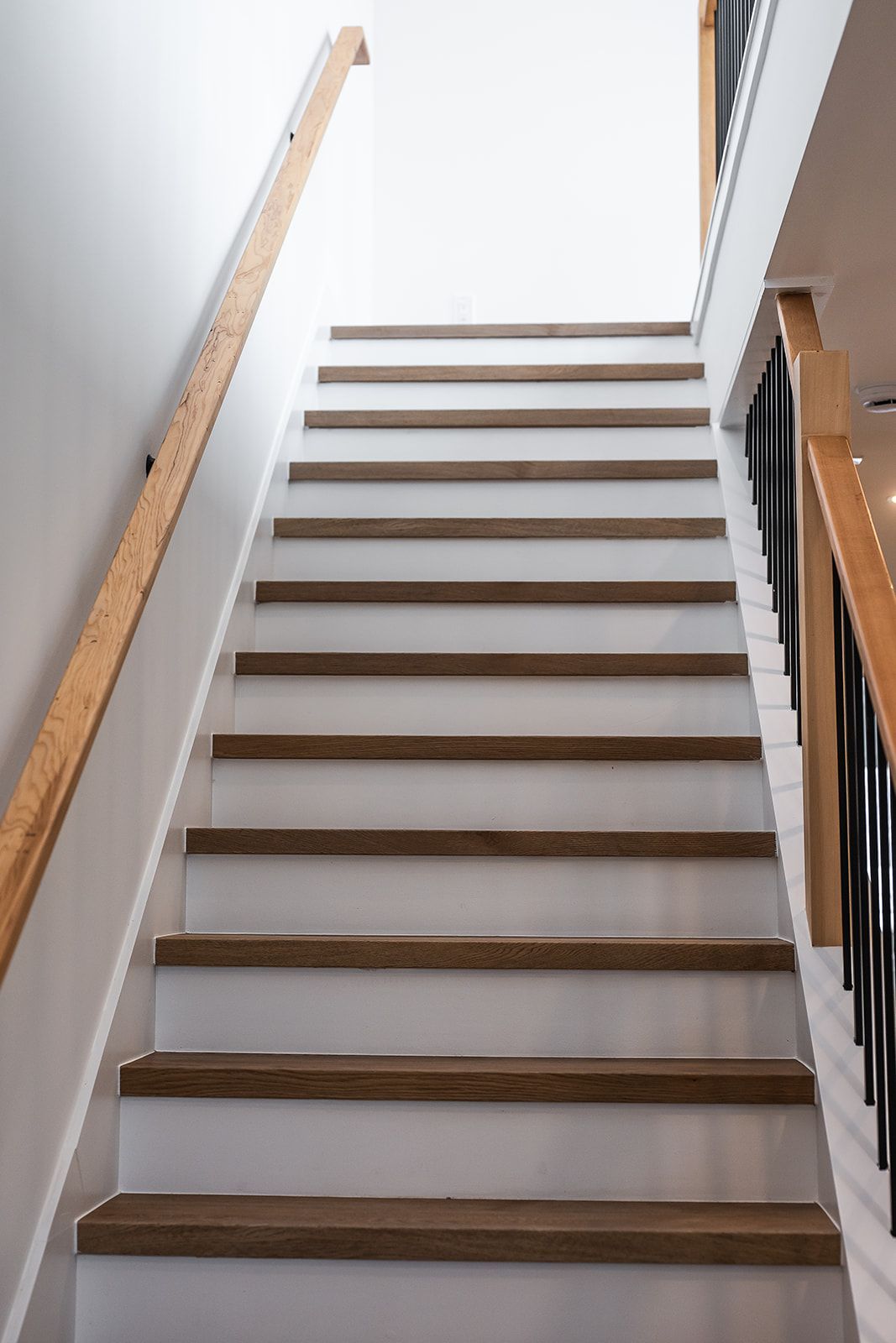 Wooden staircase with light-colored steps and white risers, leading upwards towards a bright, open ceiling.