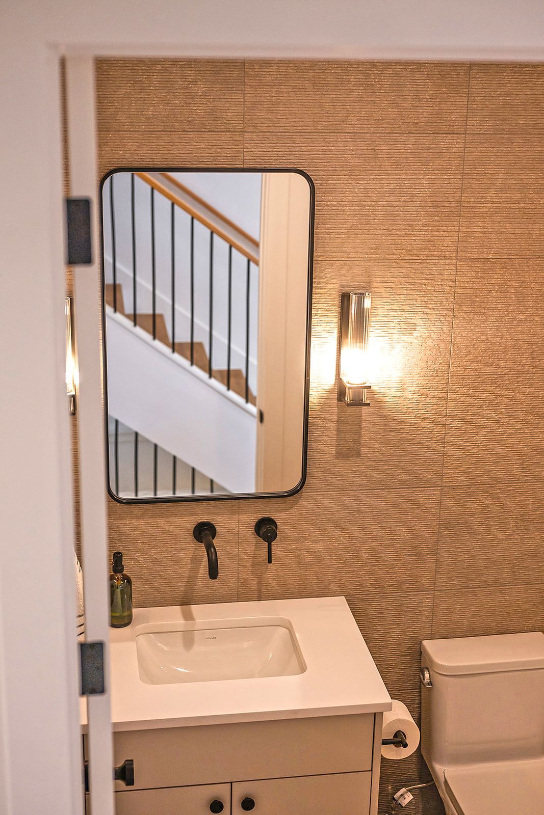 Bathroom with rectangular mirror, black fixtures, and textured tan wall. White vanity and toilet.