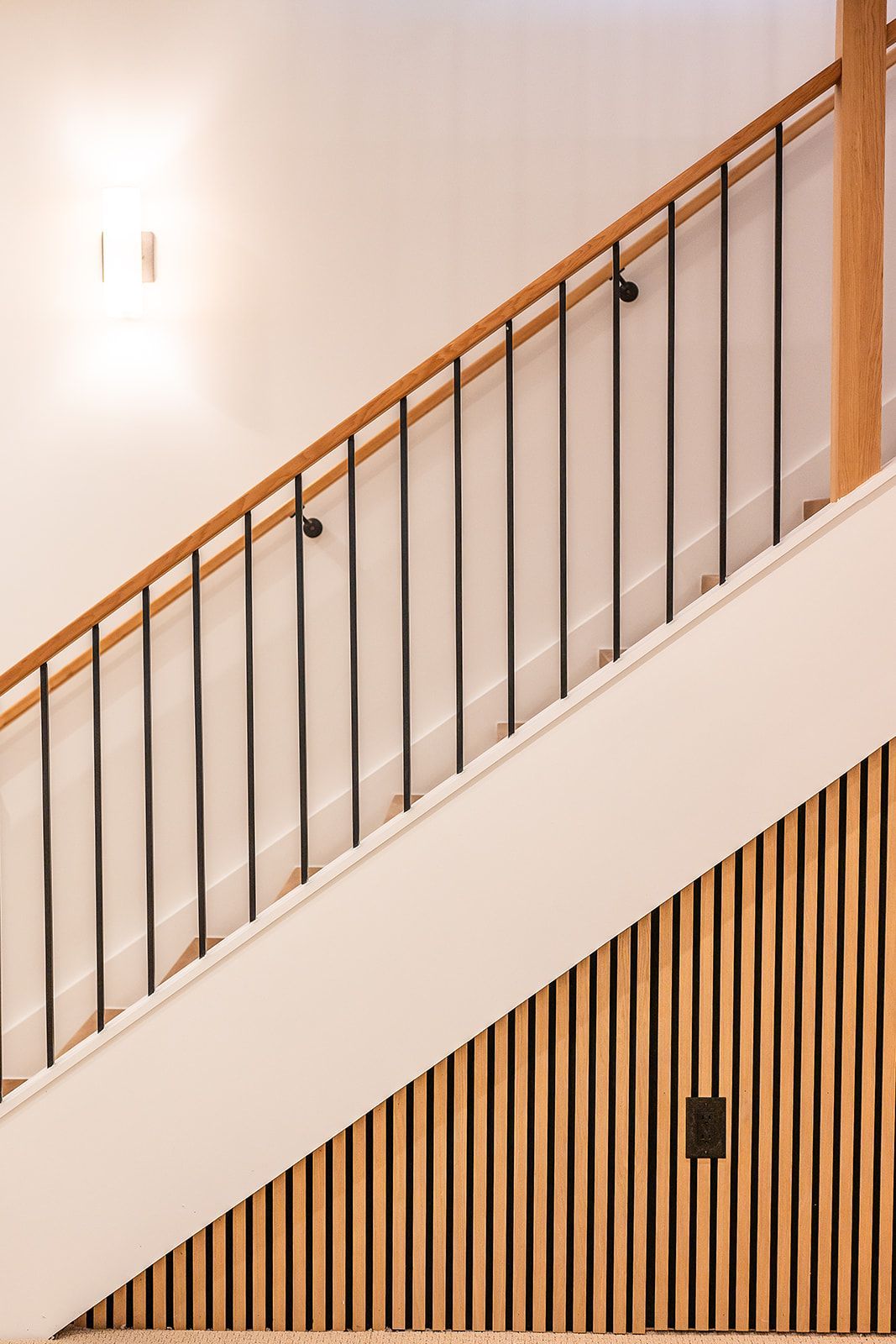 Staircase with wooden handrail, black vertical bars, and slatted wood paneling on the wall.