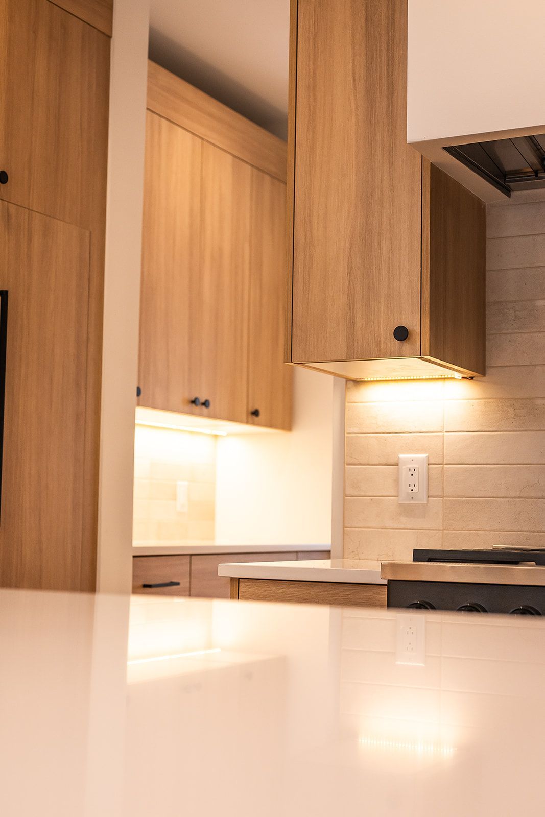 Modern kitchen with light wood cabinets, white countertops, and warm lighting.