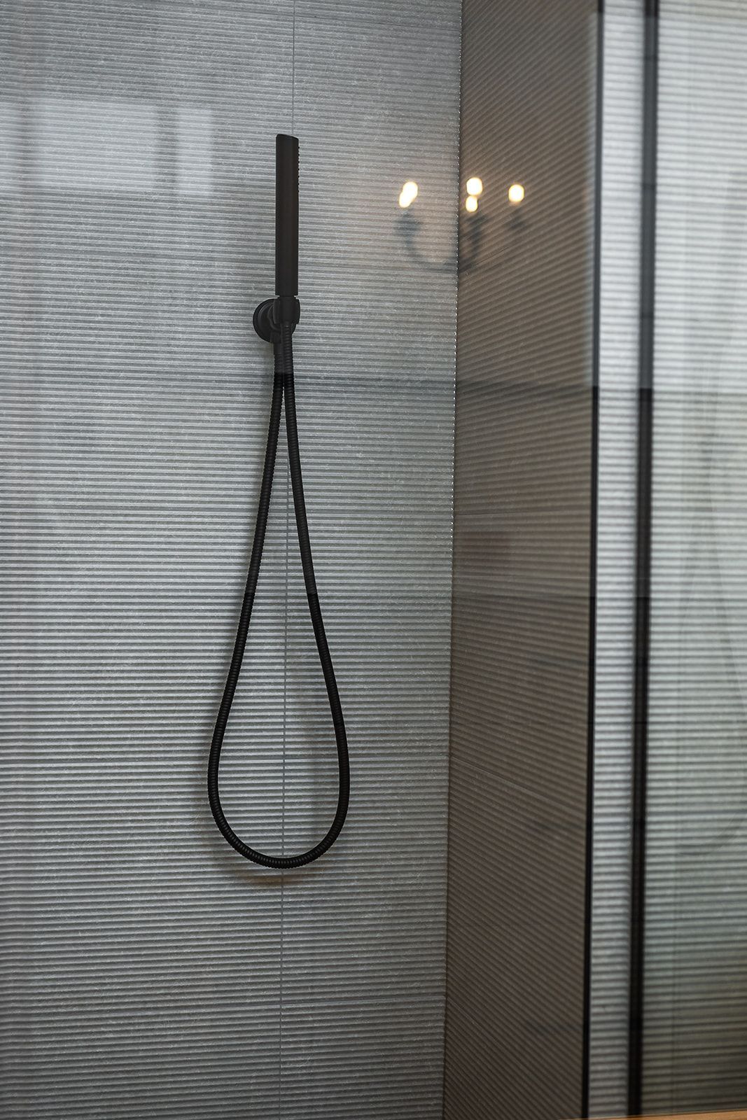 Black shower head with a looped hose against a textured gray wall, next to a window.