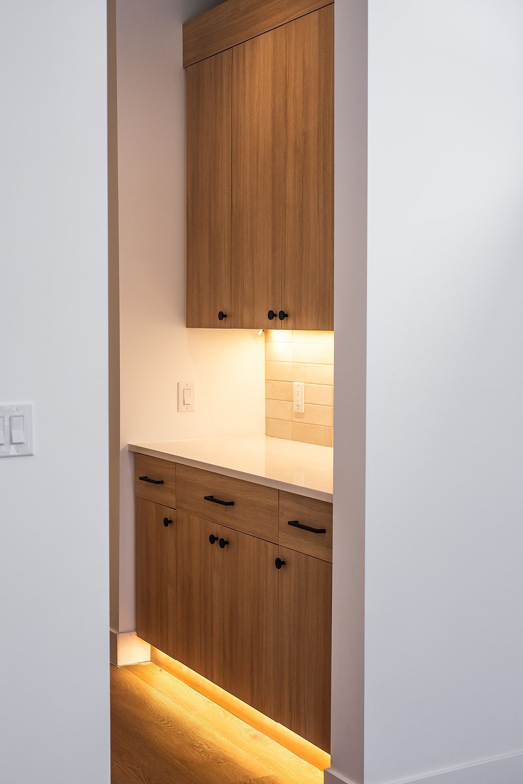Built-in wooden cabinets with under-cabinet and toe-kick lighting in a small recessed space.