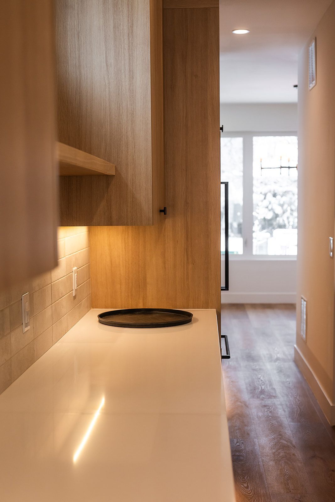 Kitchen counter with wooden cabinets, a black tray, and hallway view with a window.