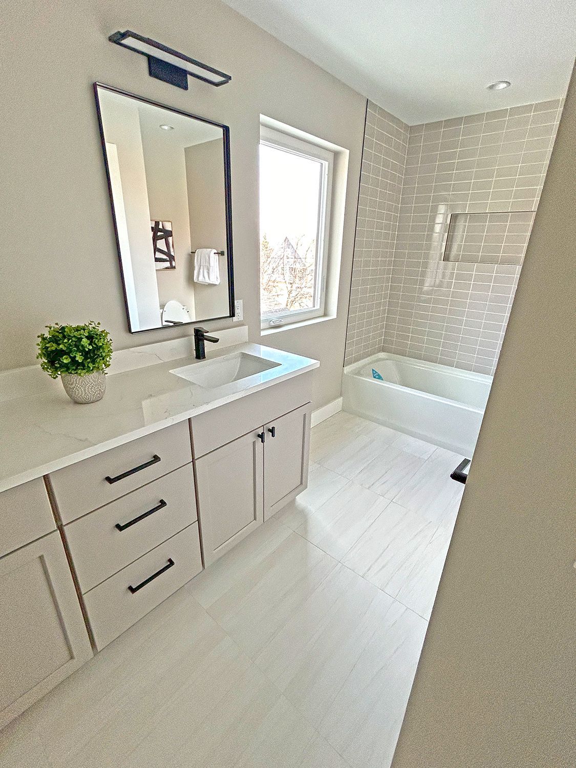 Modern bathroom with vanity, sink, mirror, bathtub, and tile. Light color scheme.