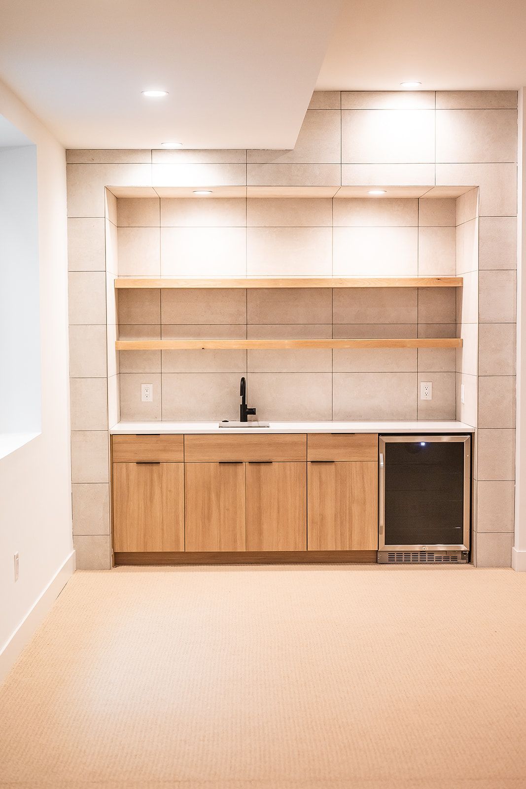 A built-in wet bar with wooden cabinets, shelves, and a mini-fridge in a neutral-toned room.