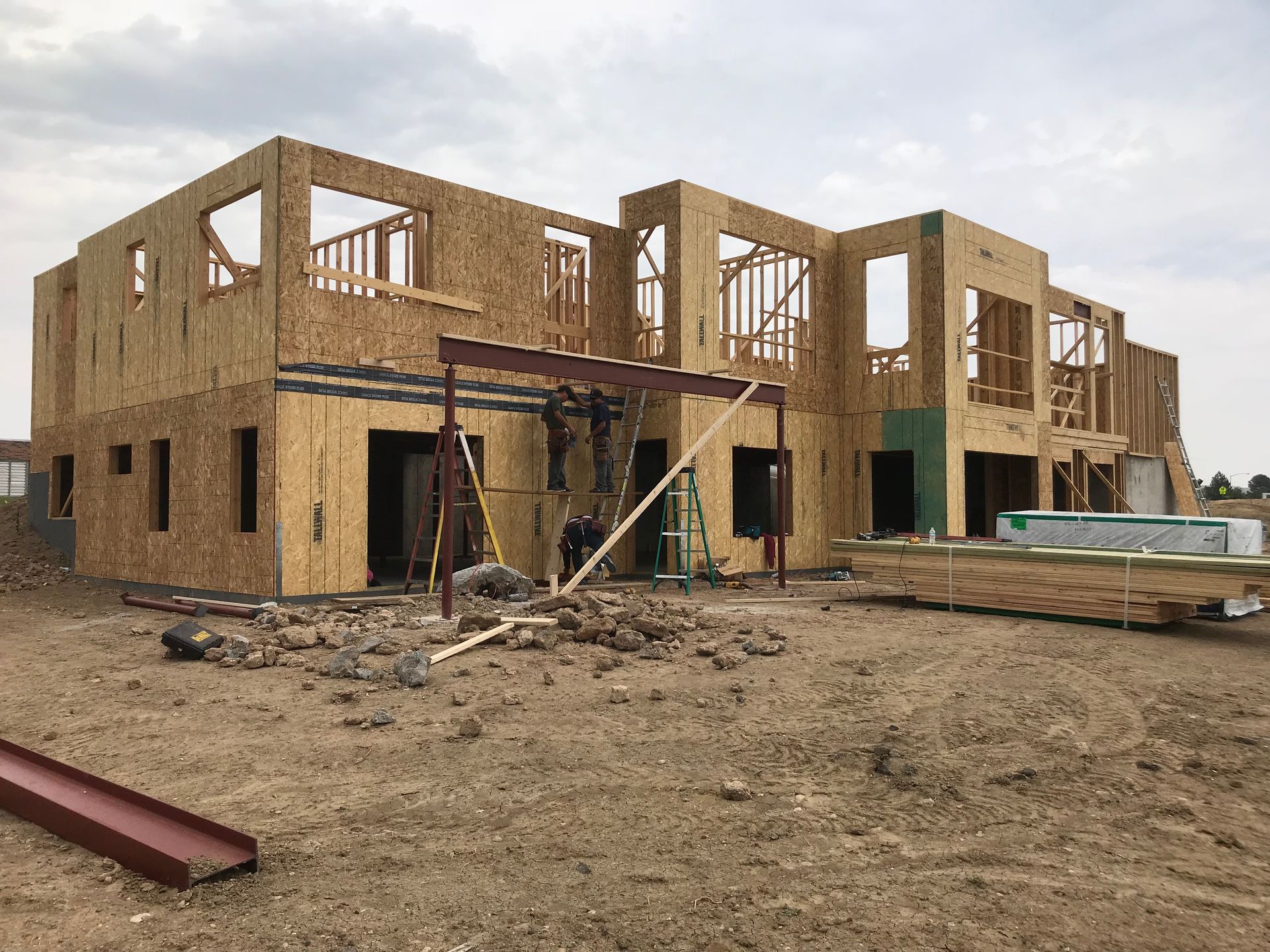 Wood-framed building under construction on dirt ground; exterior walls and window frames visible, cloudy sky.