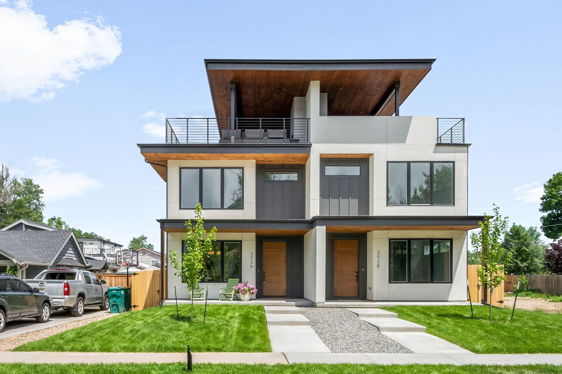 Modern duplex with light gray and wood accents, green lawn, blue sky.