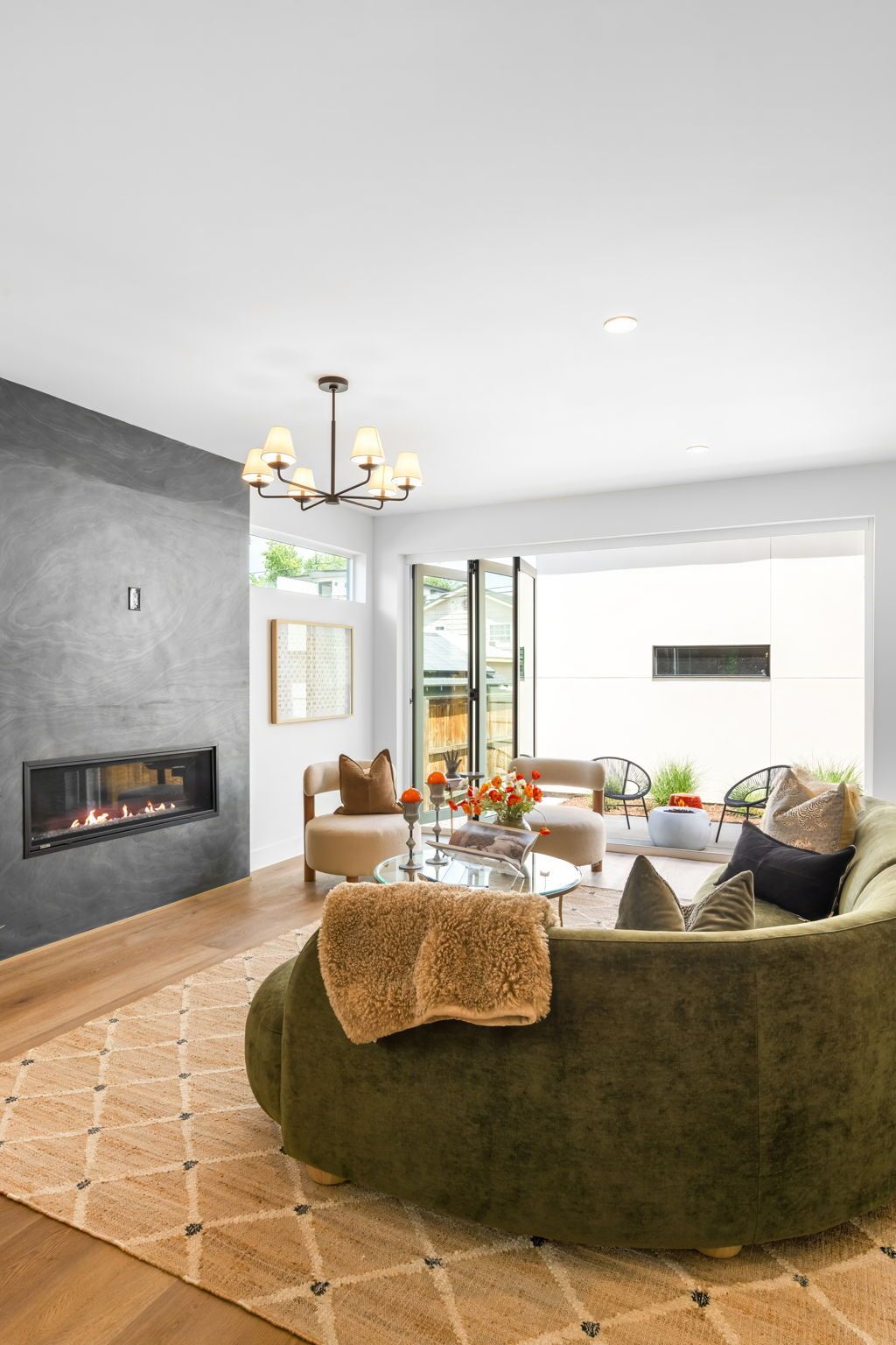Living room with olive green curved sofa, fireplace, and open doors to patio.