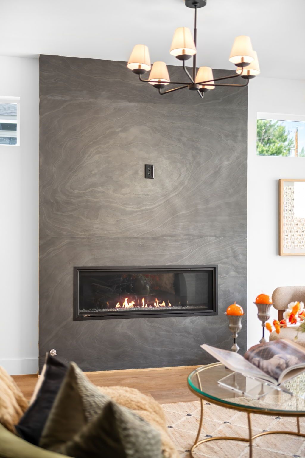 Modern fireplace with flames, dark grey wall, chandelier, and a living room setting.