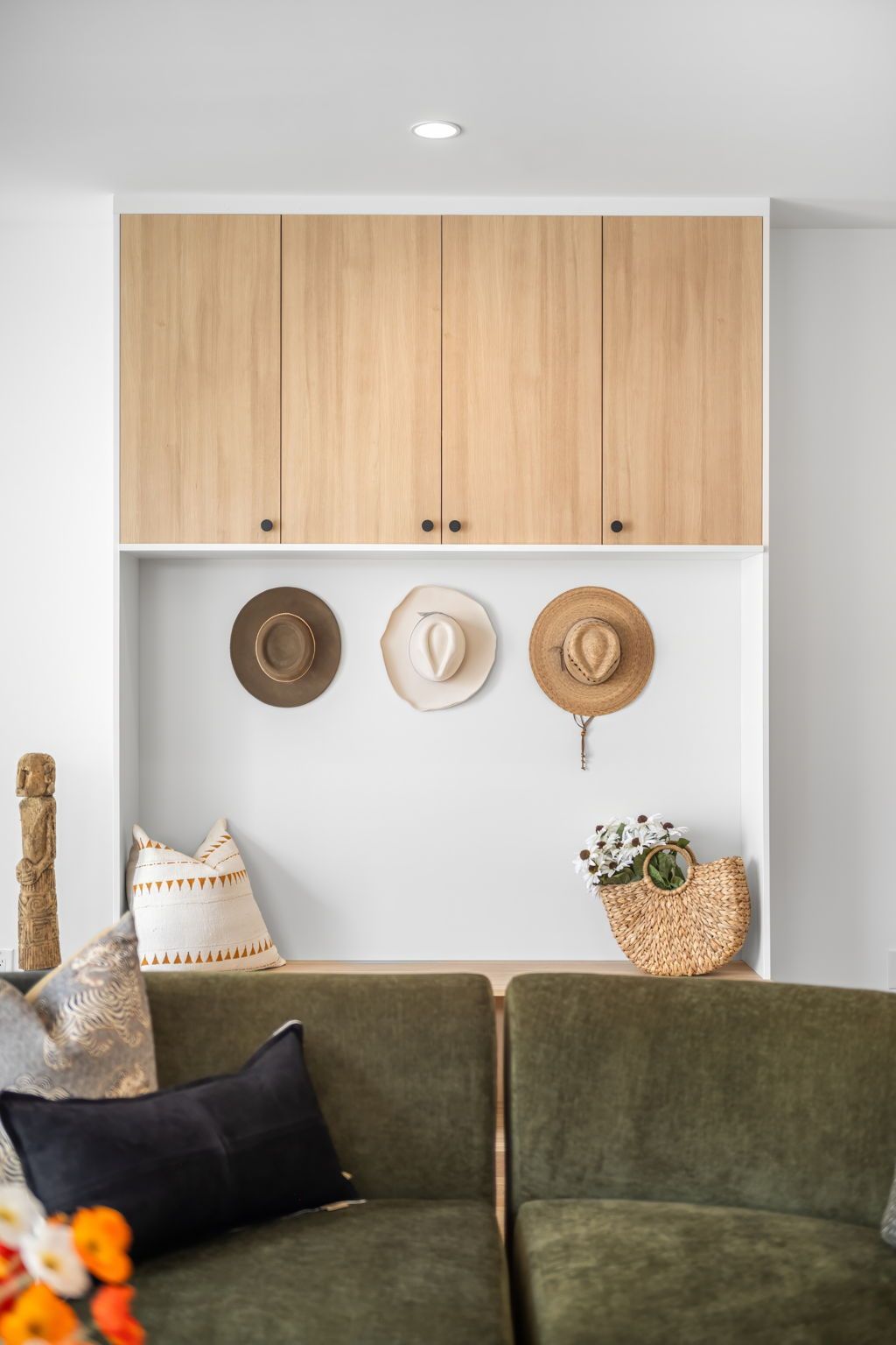 Built-in storage with light wood cabinets, hats, and a green sofa.