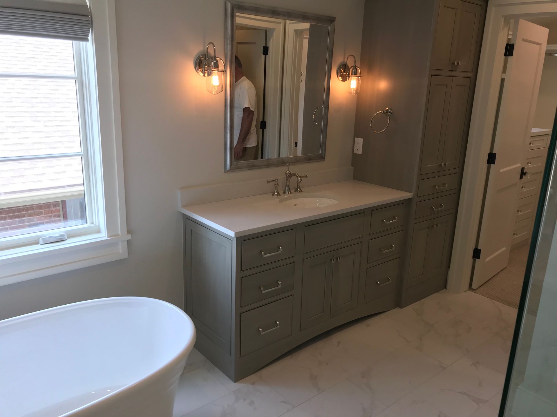 Bathroom with a white tub, light gray vanity, mirror, and tall storage cabinet.