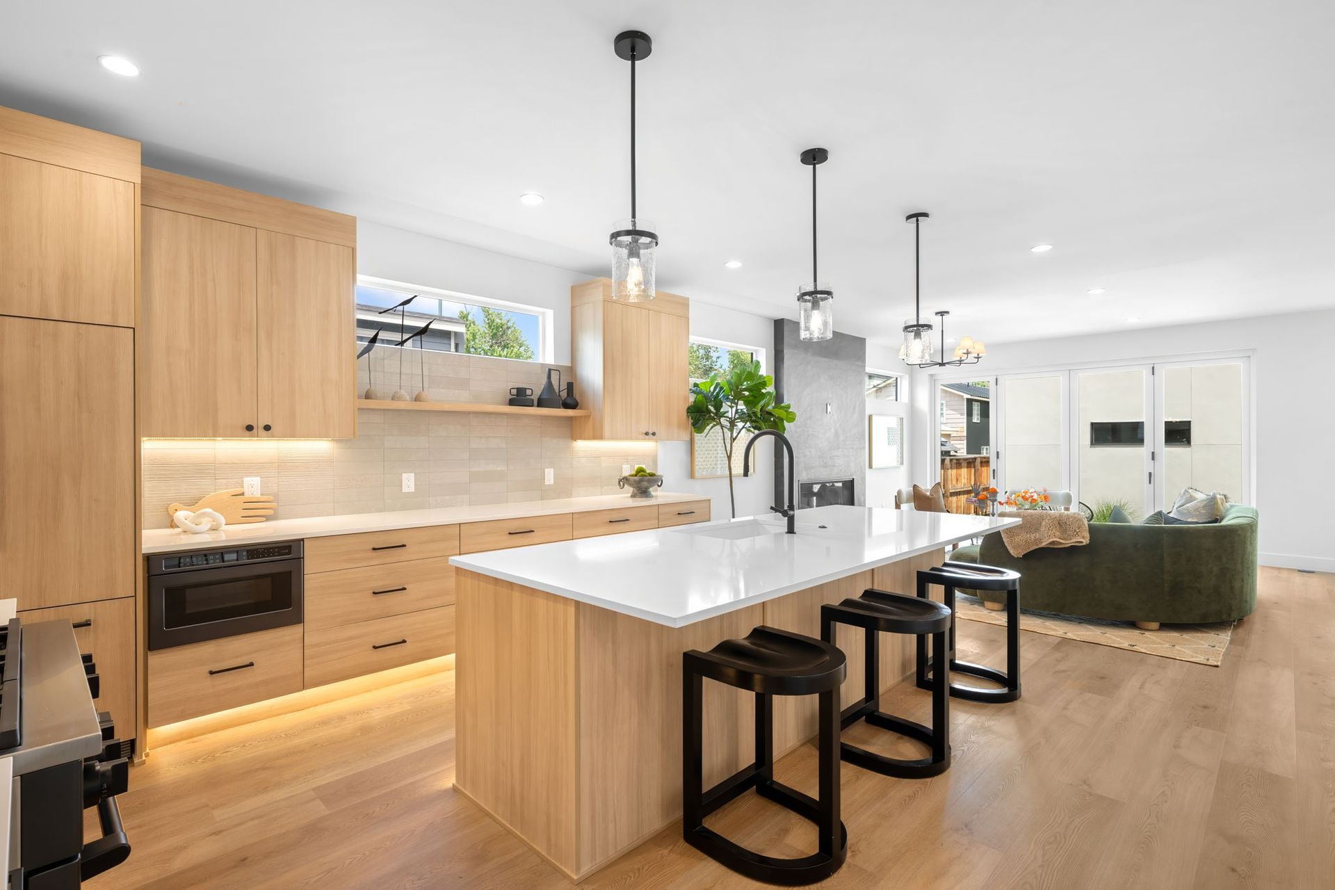 Modern kitchen with light wood cabinets, white countertops, and black bar stools.