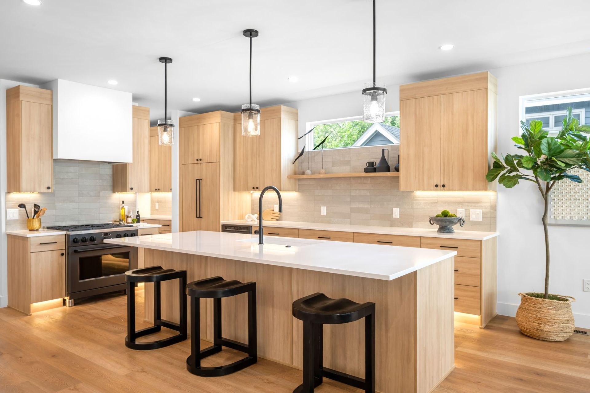 Modern kitchen with light wood cabinets, white countertops, black accents, and a large island.