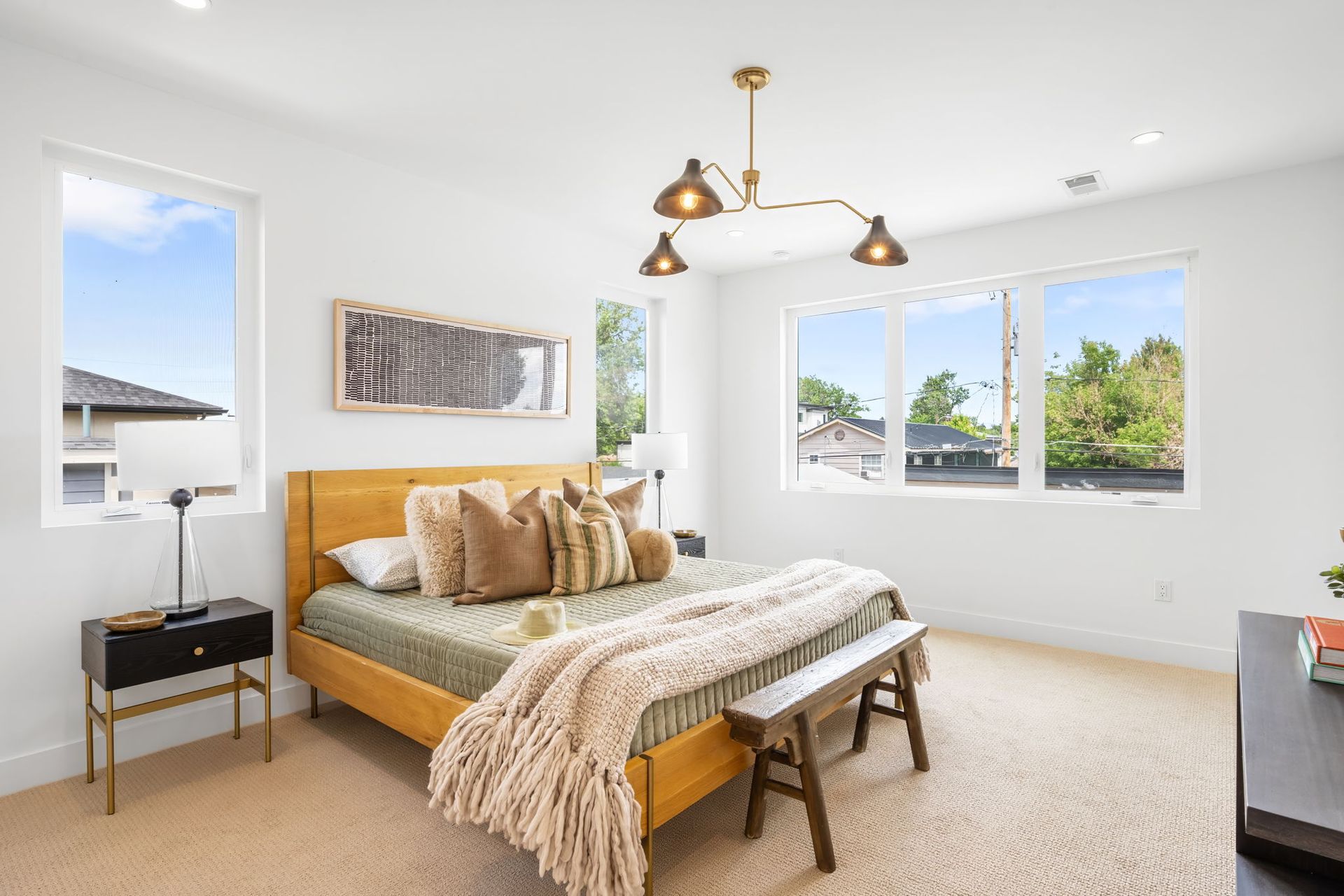 Bedroom with a light wood bed, beige carpet, and a modern brass chandelier.
