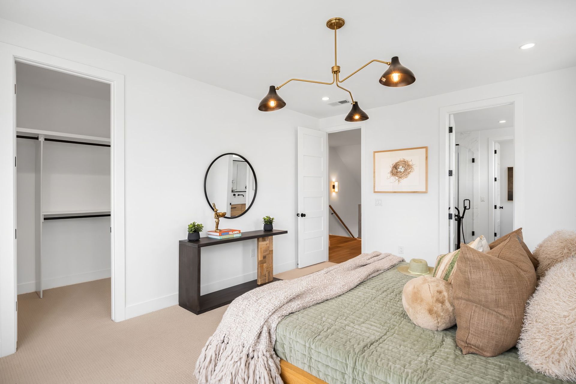 Bedroom with bed, closet, and modern decor: brass light fixture, round mirror, white walls.
