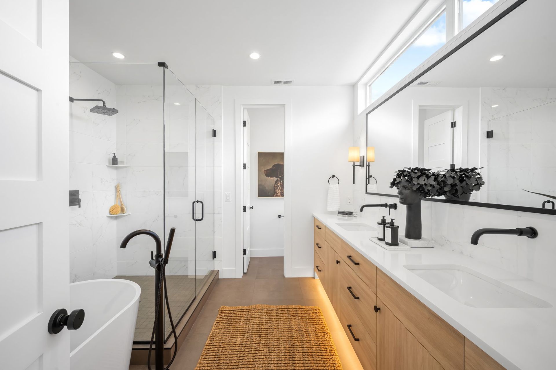 Modern bathroom with a glass shower, soaking tub, and long wooden vanity with black accents.